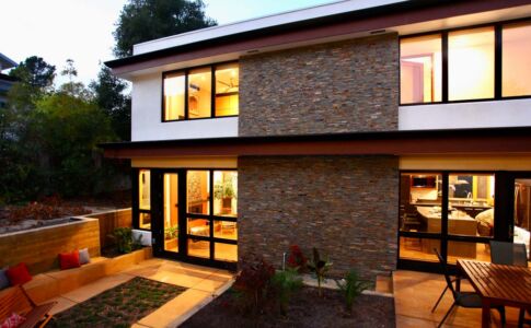 Stained concrete patios extend directly from corresponding indoor spaces, and the lines of the hearth and interior stairs flow seamlessly to the exterior -- tying indoors and outdoors together. Photo of home and patio in evening light