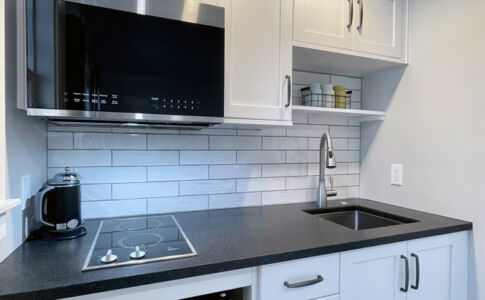 Within its 5' wide addition, the small but mighty kitchen includes a two-burner induction cooktop, mini fridge, microwave with exhaust vent, and sink. New kitchen addition at garage conversion ADU