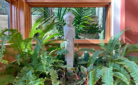 A replica Garden Sprite from Frank Lloyd Wright's demolished Midway Gardens keeps watch over the home from her perch in the living room's built-in planter. A corresponding outdoor planter just beyond the windows ties indoors and outdoors together visually. Photo of statue among plants